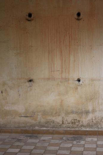 A stone wall seemingly stained with blood and marked with bullet holes: the scene of an execution
