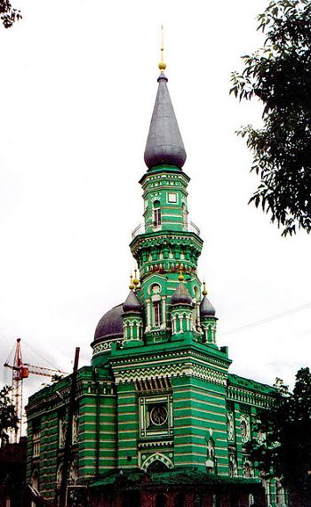 Green-and-gold-coloured mosque in the Russian city of Perm, with grey onion domes and a red crane in the far background 